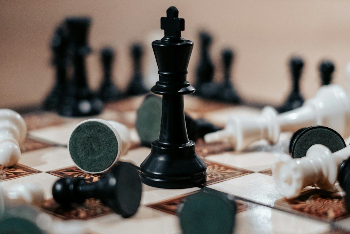 Image shows fallen chess pieces on a board; only the black King remains standing.